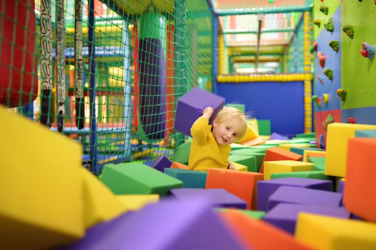Cute little boy plays with soft cubes in the dry pool in play center. Kid playing on indoor playground in foam rubber pit in trampoline. Child having fun in entertainment center.